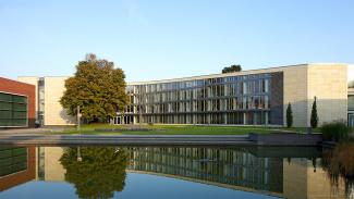 Foto von dem Hauptgebäude des Hasso-Plattner-Instituts, In der Unteren Bildhälfte ist ein Teich zu sehen mit blauem Himmel