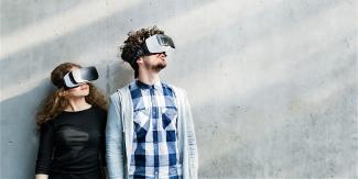 Zwei junge Erwachsene tragen VR-Brillen und blicken über die linke Schulter nach oben