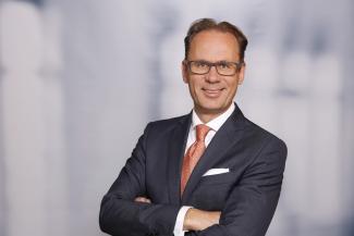 Mann mit Brille, grauem Anzug und rötlicher Krawatte