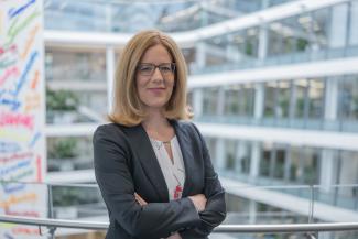 Frau mit Brille und schulterlangem blondem Haar, trägt einen dunkelgrauen Blazer
