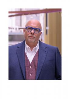 Mann mit blauen Chakett und blauer Brille sowie mit kurzem weißen Kinn- und Schnurbart