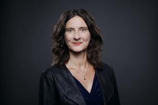 Frau mit schulterlangen dunklen Haaren vor einem dunklen Hintergrund 