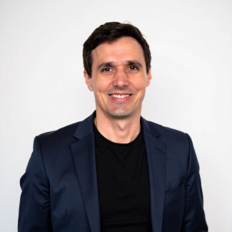 Lächelnder Mann mit dunklen Haaren in schwarzem T-Shirt unter dunklem Sakko