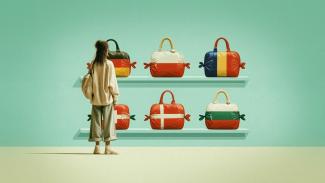 Junge Frau steht vor zwei Regalbrettern mit Reisetaschen im Design unterschiedlicher Landesflaggen